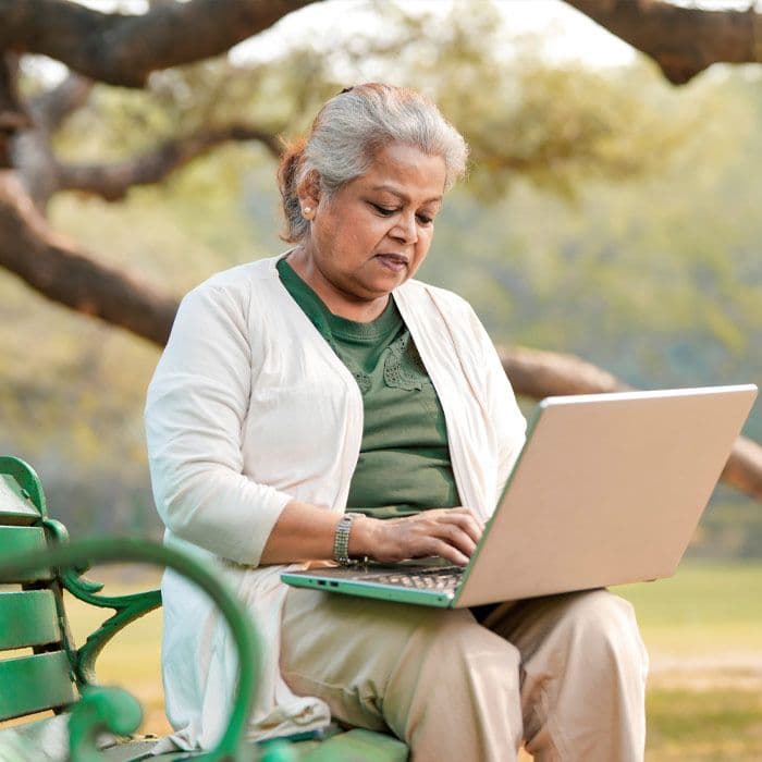 An elderly Indian woman sitting on a park bench using a computer